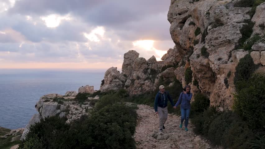 Two tourists go along the rock against the sea