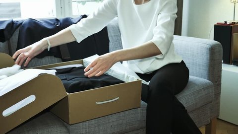 Elegant fashionable woman unpacking unboxing new cardboard with multiple clothes suits black elegant on the living room sofa - online shopping