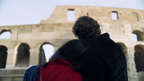 On a beautiful sunny day, a happy, loving Italian couple hug each other as they look at the Coliseum in Rome. Medium shot on 4k RED camera.