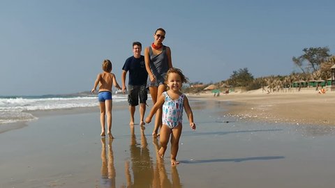 Cute little smiling child running along the beach with big happy healthy family on background and falling down .Slow motion 50Fps. 