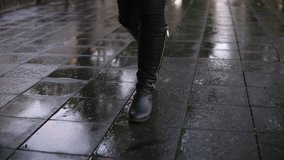 Woman take walk at autumn park walking along the pavement alley. Close up legs and shoes view. Graceful lady wear black high boots. Autumn weather, rayny, wet road. Front view