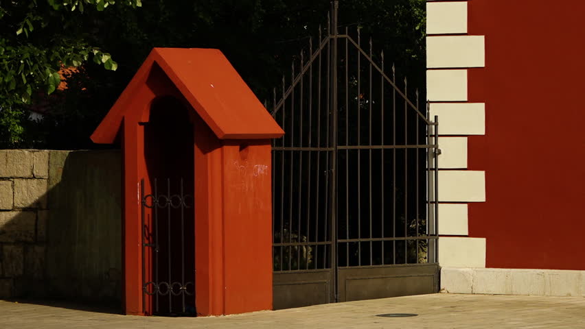 Close up of black metal fencing that secures a large brown-red and white building