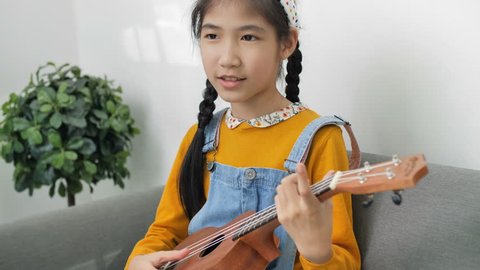 4K Little Asian child playing ukulele and singing a song
