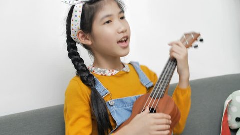 4K Little Asian child playing ukulele and singing a song