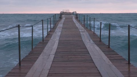 Waves splashes through the wooden pier in the sea. Beautiful seascape at sunset.