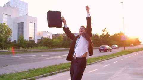 SLOW MOTION, SUN FLARE, CLOSE UP: Excited Caucasian yuppie dancing down the sunlit street after getting promoted. Happy businessman dances along the empty sidewalk on a beautiful summer evening.