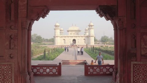 Agra, India - 10 November, 2018: Amazing view of the Tomb of Itimad-ud-Daulah (Baby Taj) through red sandstone gate. The white marble mausoleum is visible on blue sky background. Mughal architecture.