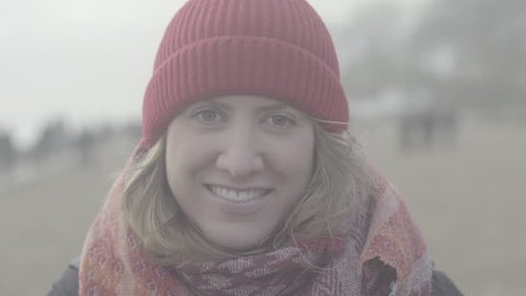 ungraded, portrait of beautiful woman smiling enjoying cloudy seaside exploring vacation lifestyle with wind blowing hair, girl looking into camera wearing red wool cap and scarf on the beach, slog2  