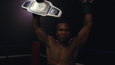 An African American boxer celebrates excitedly after winning a boxing championship. He shows off the winning Championship belt to the camera
