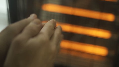 Man rubs cold hands next to a warm radiator indoors. Using household heater in an apartment or home during cold and chilly day. Palms freezing defrosting against warm heater. Cozy inside. Close up