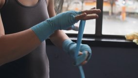 Close up of a female boxer expertly tying blue MMA hand wraps around her wrists in a gym - Powered by Shutterstock - Get 15% off with code: PIKWIZARD15