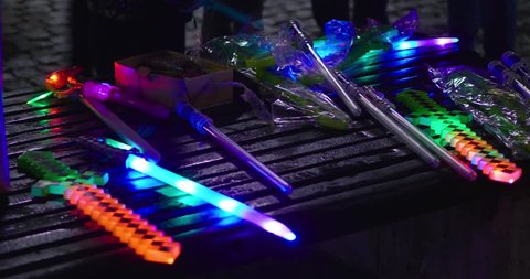 Collection of various toy light up swords laid out on wooden bench, flashing & lit up.