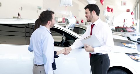 Good looking salesperson showing some cars to a couple in a car dealership
