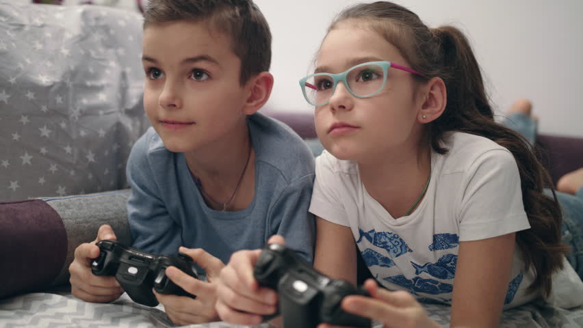 Kids playing video games at home. Brother close eyes sister. Children have fun together with joysticks in hands. Happy siblings enjoy video game | Shutterstock HD Video #1022857231