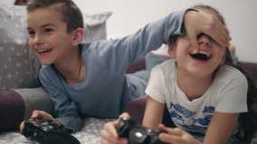 Kids playing video games at home. Brother close eyes sister. Children have fun together with joysticks in hands. Happy siblings enjoy video game - Powered by Shutterstock - Get 15% off with code: PIKWIZARD15