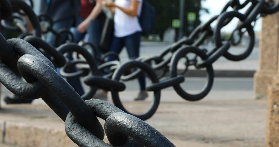 pedestrians can be seen through large black chains.