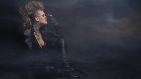 Rocker woman in leather jacket, posing on the floor in sunglasses, smoke and black background - Powered by Shutterstock - Get 15% off with code: PIKWIZARD15