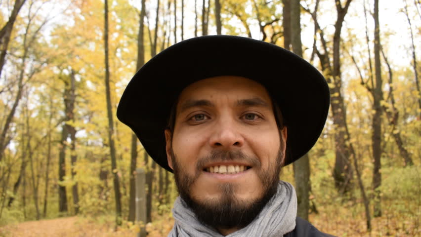 Closeup of smiling young man with beard looking at rotation camera in forest.