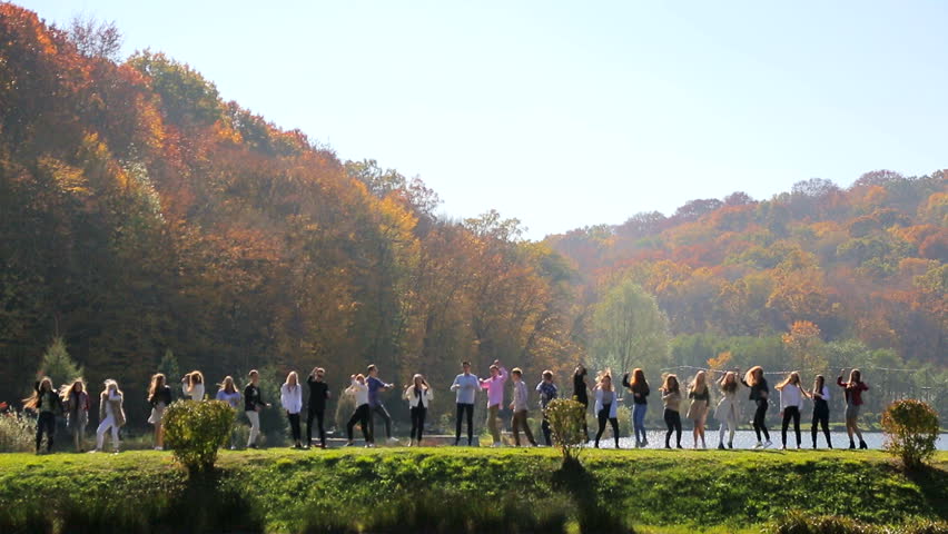 A group of happy people dancing in the park near the lake.