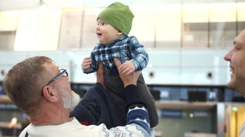 Grandpa first saw his little grandson. Mature man takes the hands of the baby. Grandfather, son and grandson. Meeting at the airport
