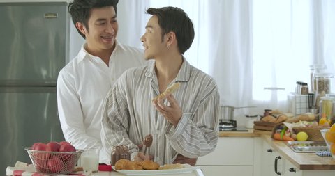 Attractive young asian gay couple having breakfast in kitchen. Man cooking breakfast for him boyfriend with attractive smiling. People with gay, homosexual, relationship concept.
