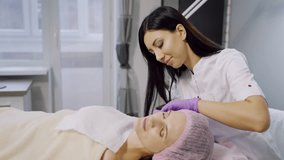 A cosmetologist makes injections for a woman in a beauty center. The client is laying on the couch during the procedure. Mesotherapy.