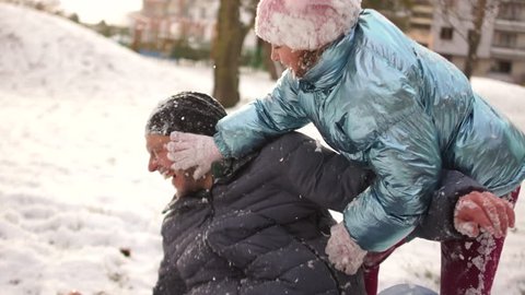 Serious snow fight. A girl smears snow on her fathers face. Man laughs