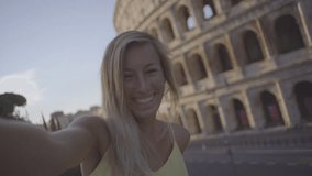 Cheerful young woman in Rome taking a selfie in front of the Colosseum at sunrise enjoying Italian city travel in Summer. Girl on vacations in capital city of Italy - 4K resolution 