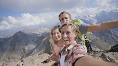 Three young people hiking in Summer and taking a selfie portrait on mountain top at the summit 
