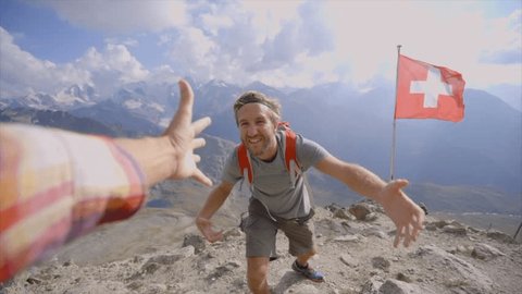 Point of view of hiker pulling out hand to help teammate reach the summit. Young man hiking in the Alps, hand reaches out to help. Helping hand concept. Achievement and success at mountain top. 