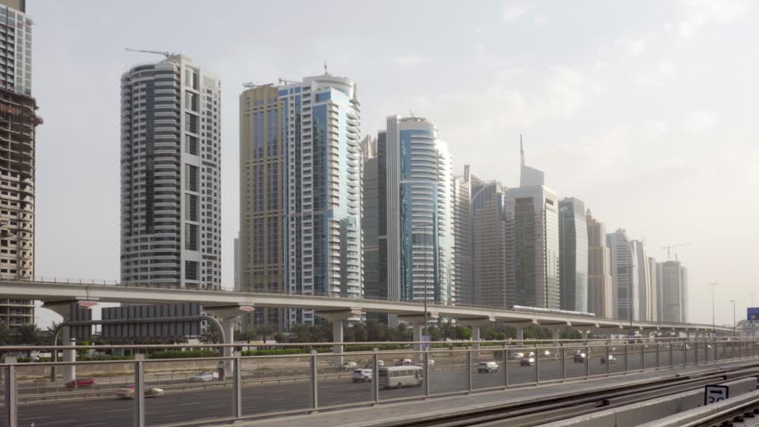 Train passing above Sheikh Zayed Road in Dubai, United Arab Emirates (UAE). Amazing view of the highway and elevated viaduct of the Red Line on high-rise buildings background.