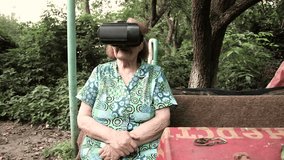 Senior woman in virtual reality glasses outdoors. Elderly woman enjoying goggles virtual reality in the garden. Grandma is watching a film with glasses VR. Senior Women tries virtual reality.