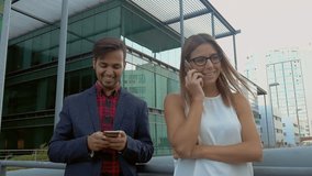 Young business people using cell phones on street. Smiling young woman talking by mobile phone and handsome man using smartphone while standing together outdoor. Communication concept