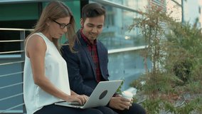 Young business people using laptop outdoor. Handsome smiling man holding coffee to go and looking at beautiful girl using laptop computer. Technology concept