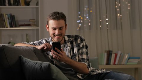 Amazed man finding good news on smart phone in the night sitting on a couch at home