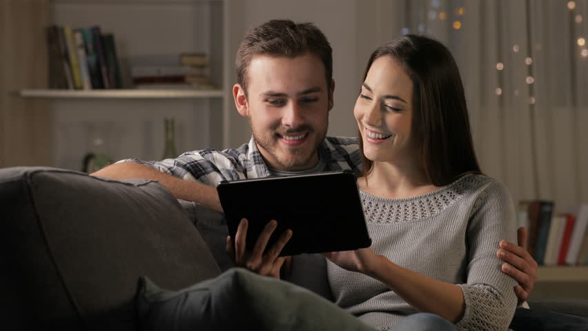 Happy couple in the night browsing tablet content sitting on a couch at home Royalty-Free Stock Footage #1022901766