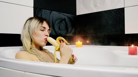 An attractive woman sits in the bathroom and with the pleasure of eating it.  A girl eats a banana after a hard day