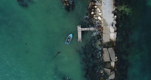 4k aerial video of lonely fishing boat and wooden pier in turquoise ocean, sea. Top view
