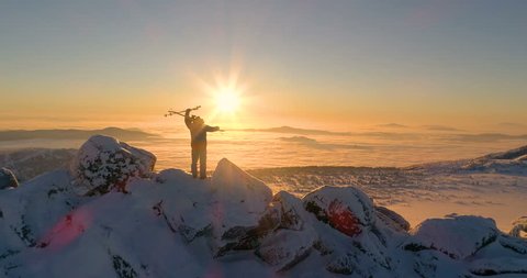 aerial view: skier on the mountain peak, skiing on his shoulder and big win position. sunrise, sunset. mountain valley. above the clouds. stock video footage. back light. camera goes linearly forward