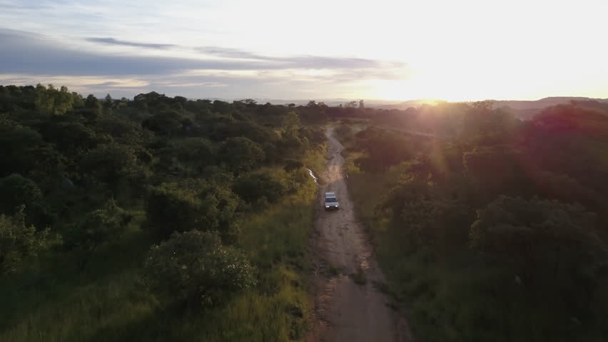 Aerial View of a Beautiful Sunrise over a Small Car Driving on a Bumpy Dirt Road through a Lush Forested Landscape in Rural Zimbabwe, Africa, Forward Movement