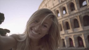 Cheerful young woman in Rome taking a selfie in front of the Colosseum at sunrise enjoying Italian city travel in Summer. Girl on vacations in capital city of Italy ;SLOW MOTION 