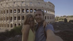 4K Selfie portrait of young couple in Rome enjoying travel in Italy and capturing a photo in front of the famous Colosseum- Two people having fun in Italian capital city 