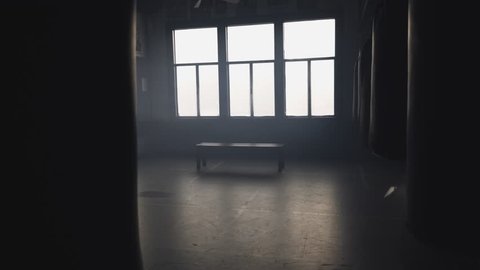 Panning shot from the inside of a hazy boxing gym, filmed behind punching bags