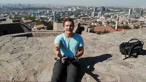 Aerial of adventurer on Ankara castle in Turkey. Tourist sitting on wall in cityscape drone shot flying away. Closeup to wide shot of Ankara city buildings. Tourism in old ancient Turkish tower.