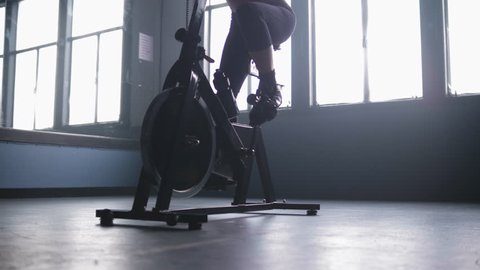 Low panning shot of a woman cycling on an indoor spin bike in a gym