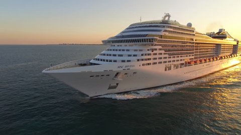 Miami, USA – January 19, 2019: Aerial drone view of large cruise ship leaving Miami harbor, sailing at sea during sunset, warm orange and red color