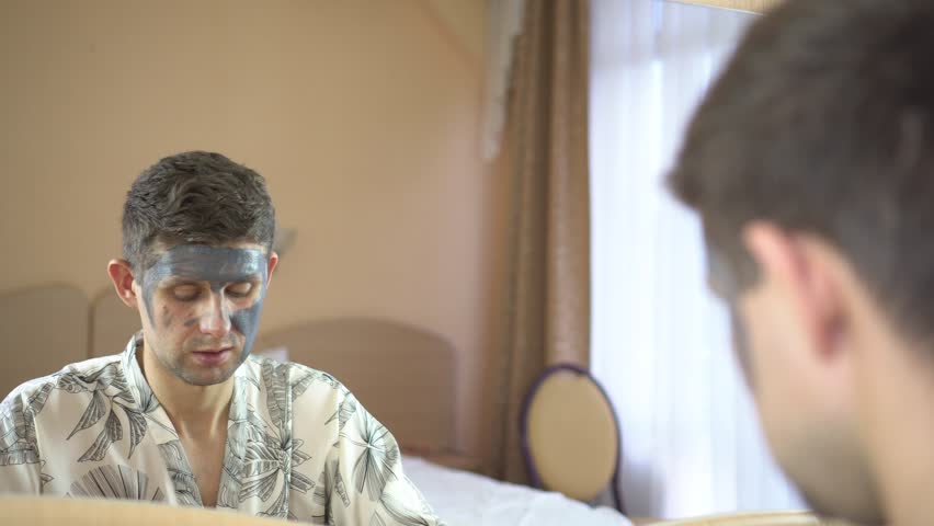 A young man uses a cream cosmetic mask for the face. Skin care.