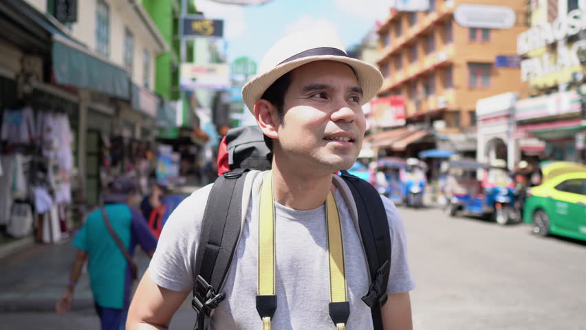 Amazed excited Asian male tourist backpacker traveling solo on Khao San road Bangkok Thailand in summer vocations
