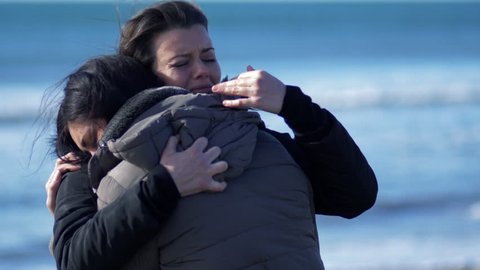 Two women crying hugging each other in winter in front of the ocean super slow motion