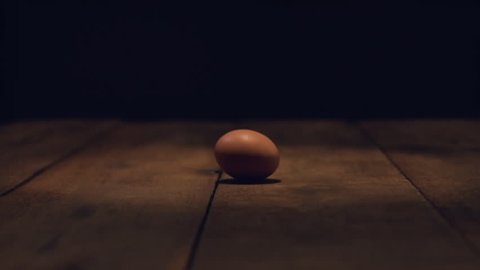 Slow motion footage of an egg rolling on a wooden table 